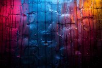 Colorful abstract background with water drops on glass surface creating vibrant gradient from pink through blue to orange, with dramatic lighting and bokeh effect.