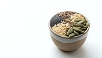 Healthy superfood bowl with chia seeds, quinoa, pumpkin seeds and mixed grains for nutritious breakfast or snack preparation on white background.