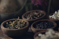 Aromatic dried herbs and tea leaves in rustic clay bowls on wooden surface, moody dark photography with natural lighting for wellness and spa concepts.