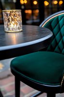 Elegant restaurant interior with emerald green velvet chair and dark wooden table, illuminated by crystal candleholder creating warm ambient atmosphere.
