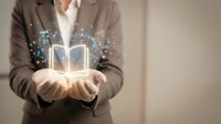 Businesswoman in brown blazer holding glowing book icon with sparkling light effects, representing digital learning, knowledge sharing, and online education for corporate training concepts.
