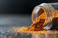 Ground turmeric powder spilling from glass jar on dark surface, vibrant orange spice with selective focus and soft lighting creates dramatic culinary scene.