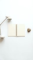 Minimalist workspace with open spiral notebook, modern desk lamp and decorative stone on clean white background for creative projects and planning.