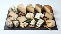Gourmet cheese platter with variety of artisanal cheeses, nuts and crackers on dark slate board isolated on white background for culinary design.