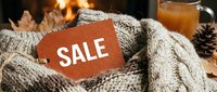Cozy knit sweater with a sale tag near a warm fireplace, autumn leaves and hot drink in background, seasonal shopping concept.