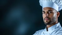 African American male chef in white uniform and hat looking confident against dark background with dramatic lighting and copy space for restaurant industry.