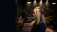 Young blonde woman wearing headphones in modern recording studio with warm lighting and professional audio equipment in background.