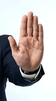 Close-up of male hand in stop gesture wearing dark navy business suit and white shirt cuff against white background for rejection, refusal, halt or warning concepts.
