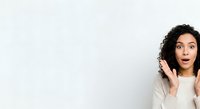 Young woman with curly dark hair and medium skin tone, wearing beige cardigan, expressing surprise with hand near face against white background.