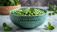 Fresh green peas in decorative turquoise ceramic bowl with mint leaves on concrete background, healthy organic vegetables for cooking and nutrition.