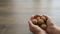 Handful of walnuts held in open palm against wooden surface. Suitable for food, nutrition, health, and wellness content.