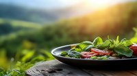 Fresh garden salad with tomatoes and herbs on rustic wooden table against blurred green mountain landscape at sunset.