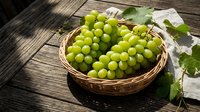Fresh green grapes in wicker basket on rustic wooden surface with vine leaves, ideal for food and agriculture marketing materials.