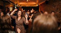 Young woman dancing and celebrating at lively indoor party with friends, warm lighting and festive atmosphere for social events and nightlife concepts.