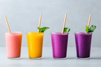 Fresh colorful smoothies in glasses with mint leaves and straws - pink strawberry, mango yellow and purple berry drinks on light background. Healthy beverages.