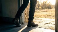 Person in boots standing in doorway with warm golden sunset light streaming through opening creating atmospheric silhouette for lifestyle and freedom concepts.