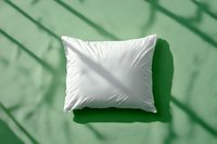 White fluffy pillow on green background with natural window shadow overlay creating geometric pattern. Clean minimal composition for bedding and home decor.