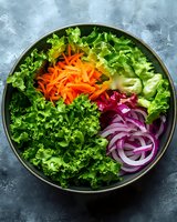 Fresh colorful salad bowl with mixed greens, shredded carrots, red onions and kale on textured background for healthy eating and nutrition concepts.