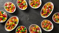 Colorful assorted candies in white bowls arranged on dark slate background. Sweet treats for parties, celebrations, and confectionery displays.