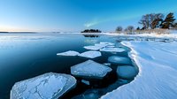 Dramatic winter landscape with broken ice floes floating on dark blue water against snowy shoreline and clear sky at dusk, natural phenomenon on frozen lake.