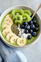 Green smoothie bowl topped with sliced banana, kiwi, blueberries, coconut flakes and chia seeds in ceramic bowl. Fresh healthy breakfast concept.