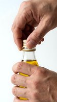 Close-up of mature male hands opening golden oil bottle against white background. Isolated stock photo suitable for culinary, wellness, and cooking design projects.