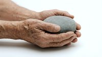 Elderly hands gently holding a smooth gray stone, symbolizing mindfulness, balance, and calm. Isolated on white background.