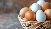 Fresh brown and white chicken eggs in rustic woven basket on wooden surface, selective focus with soft natural lighting creates appetizing farm-to-table composition.