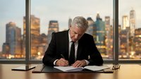 Senior executive businessman signing important documents at modern office desk with city skyline view during golden hour for corporate business deals.