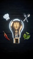 Glowing light bulb surrounded by chef hat, cutlery, chili pepper and herbs on dark background representing culinary creativity and cooking inspiration.