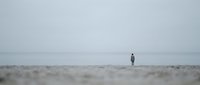 Solitary figure standing on vast sandy beach in overcast weather, conveying isolation and contemplation for editorial and lifestyle projects.