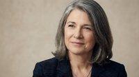 Professional mature woman with gray hair in business suit smiling confidently against neutral background for corporate and leadership concepts.