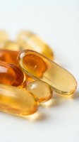 Golden gel capsules and liquid supplements in amber and clear tones with blurred fruit background, suitable for health, wellness, nutrition and pharmaceutical marketing materials.