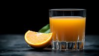 Fresh orange juice in elegant glass with sliced citrus fruit and green leaf on dark background, dramatic lighting creates appetizing beverage composition.
