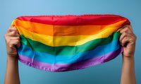 Hands holding up colorful rainbow pride flag against blue background, representing LGBTQ+ community support, equality, and celebration of diversity.
