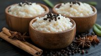 Steamed white rice in wooden bowls garnished with black peppercorns, served with cinnamon sticks and star anise on dark wooden surface. Asian cuisine background.