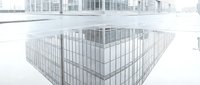 Empty metal cage or pen structure on white floor with modern buildings in blurred background, suitable for industrial, construction, storage, or architectural design projects.