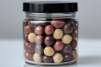 Colorful chocolate candy balls in glass jar with black lid on white surface, mix of milk, dark and white chocolate spheres for confectionery and desserts.