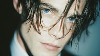 Young man with wet dark hair and piercing blue eyes in moody lighting for fashion and beauty concepts.