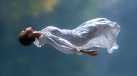 Young African American woman in flowing white dress floating weightlessly against dark blue background, ethereal and dreamy artistic portrait for creative projects.