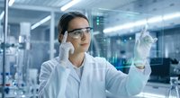 Young Asian female scientist in safety glasses examining test tube in modern laboratory conducting research experiment for pharmaceutical development.