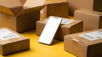 Smartphone with blank screen surrounded by cardboard shipping boxes on yellow background for e-commerce delivery and online shopping concepts.