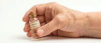 Senior adult hand holding small essence bottle on white background, suitable for skincare, wellness, and beauty product marketing materials.