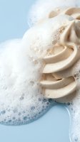 Creamy beige cosmetic foam cleanser with rich lather on a light blue background, showcasing luxurious texture for skincare and beauty product advertising.