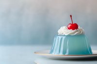 Light blue jelly dessert topped with whipped cream and a red cherry on a plate, soft pastel background, elegant food styling.