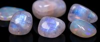 Rainbow moonstone gemstones with iridescent blue flash adularescence effect on black background for jewelry making and crystal healing practices.
