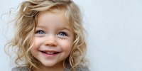 Joyful young child with curly blonde hair and bright blue eyes smiling against white background, perfect for family, happiness, and childhood concepts.