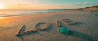 Word LOVE written in sand on a sunny beach at golden sunset with a turquoise glass heart, romantic seaside scene for valentines day.