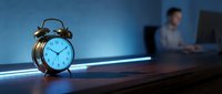 Vintage alarm clock on desk with blurred businessman working late at night in modern office, time management and work-life balance concept.