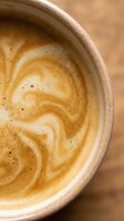 Overhead view of creamy latte with latte art swirl in ceramic cup on wooden surface, suitable for coffee shop menus and beverage marketing.